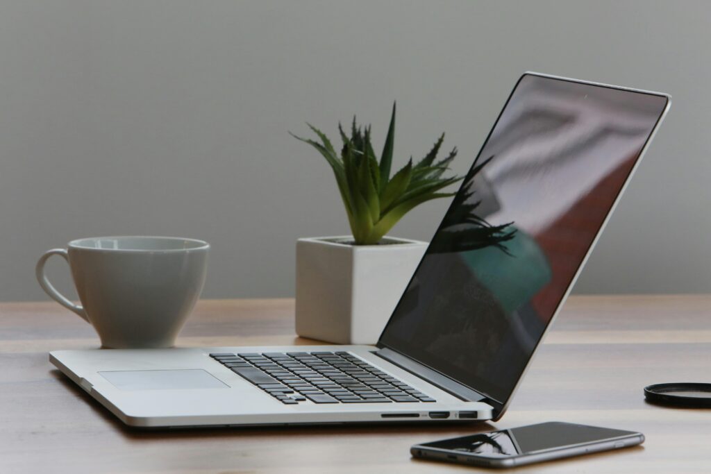 Silver laptop on a desk, next to a mug of coffee, a phone, and a potted plant, all in a very professional clean setting.